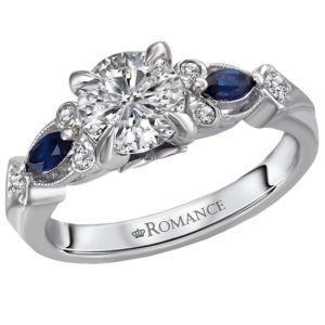 This expertly hand-crafted 14kt white gold ring accented with milgrain detail, displays brilliant cut sapphires and round diamonds surrounding the center claw prong setting that will accommodate a round 6.5mm diamond (D .09 carat weight; S 1/5 carat weight)