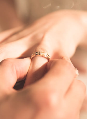 Shiny gold wedding ring on finger, close-up jewelry photo, elegant accessory for special occasions.