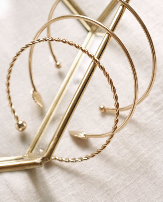 Shiny gold hoop earrings with twisted design and ball ends, displayed on a jewelry stand. Perfect for elegant accessories and fine jewelry lovers.