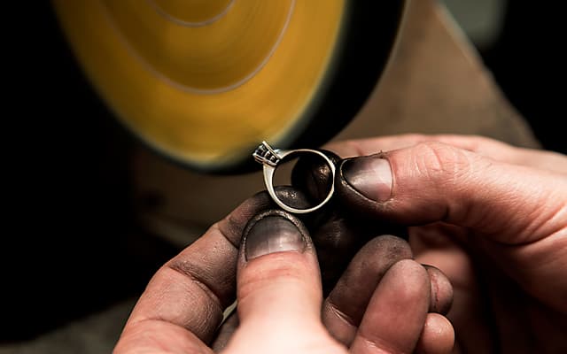 a pair of hands holding a ring being polished by a wheel